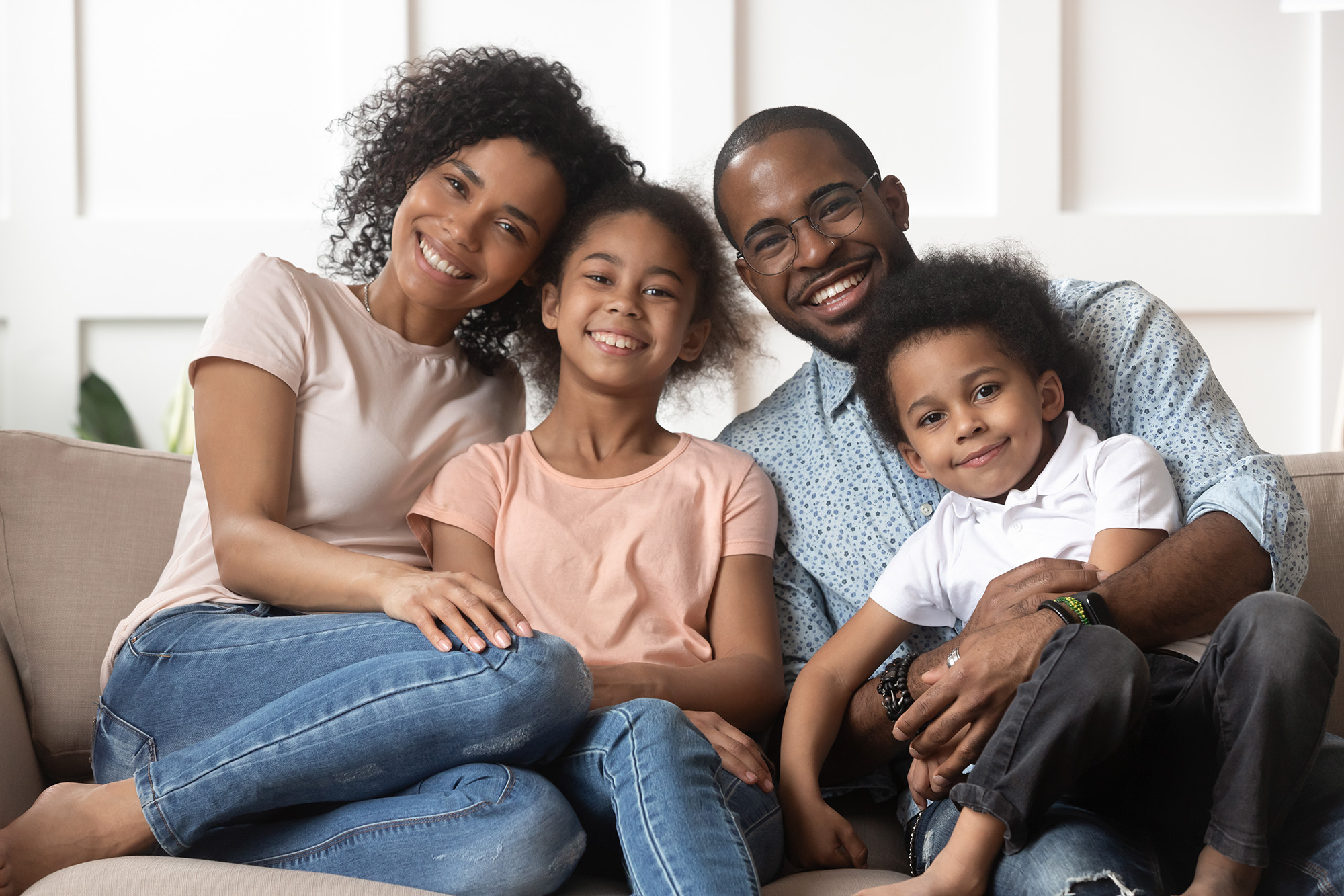 Portrait of happy young african American family with little kids sit relax on couch cuddling